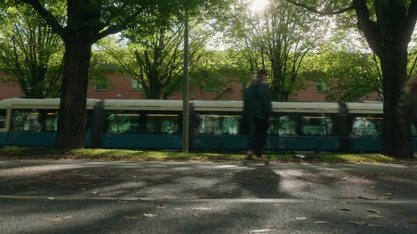 Teenagers ride their skateboards through a park while a train passes