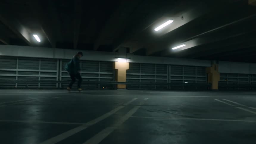A teenager is riding his skateboard in a parking garage at night
