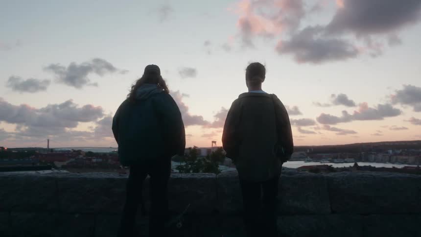 Two young men are standing at the edge of a parking garage looking down at the buildings in town