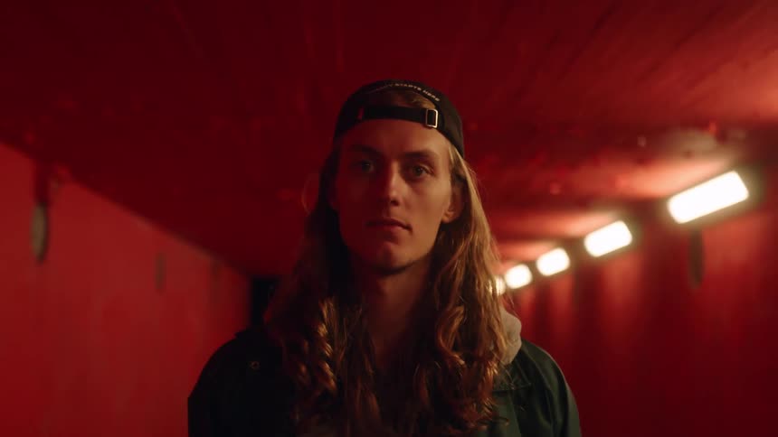 A skateboarder gazes into the camera while standing inside an indoor tunnel