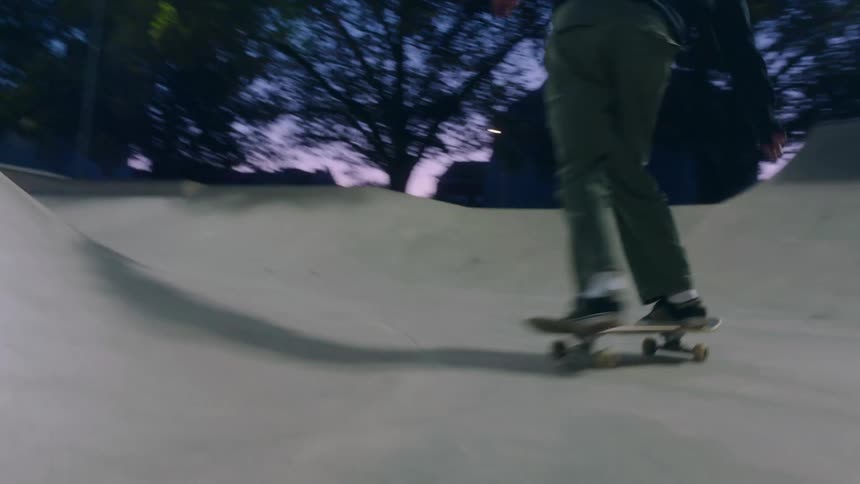 Skateboarder jumps over mound and rides up ramp in concrete bowl of skate park at night