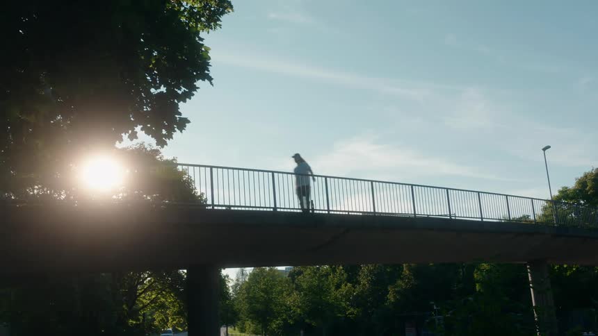 A man skateboards across a pedestrian bridge over traffic