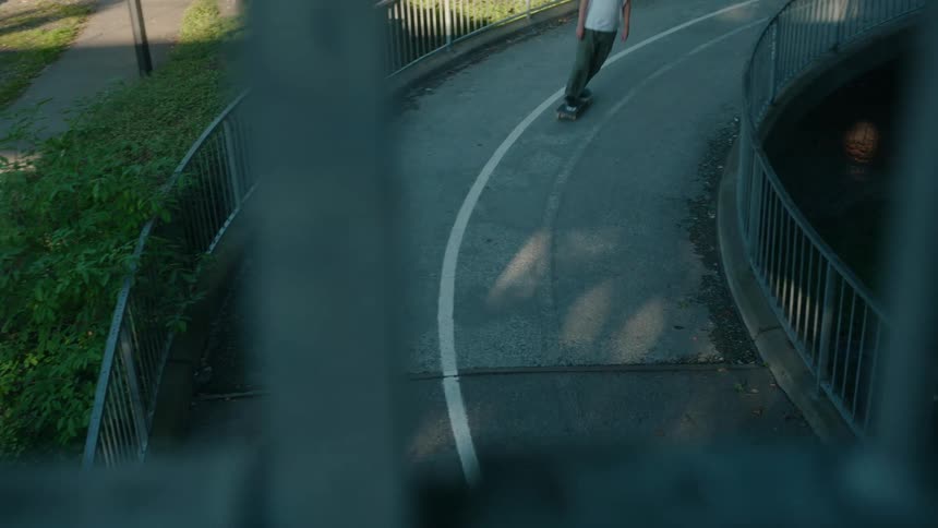 Man with brown cap white top and jeans skateboards on road