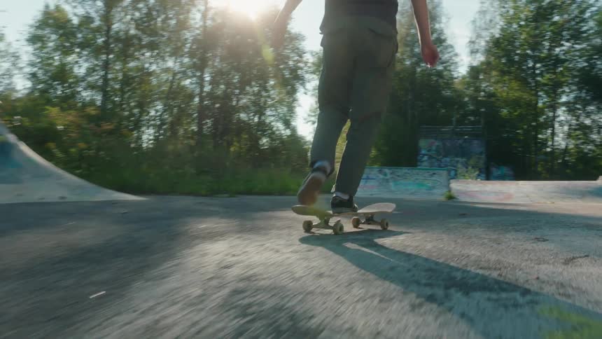 Man with long hair black t shirt green pants and black shoes skateboards in skatepark jumping