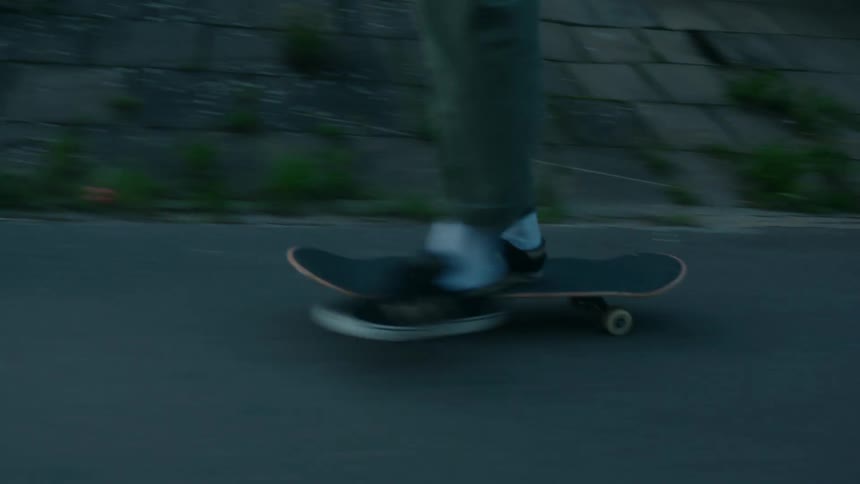 Young man exits a tunnel riding a skateboard into a town road at daytime