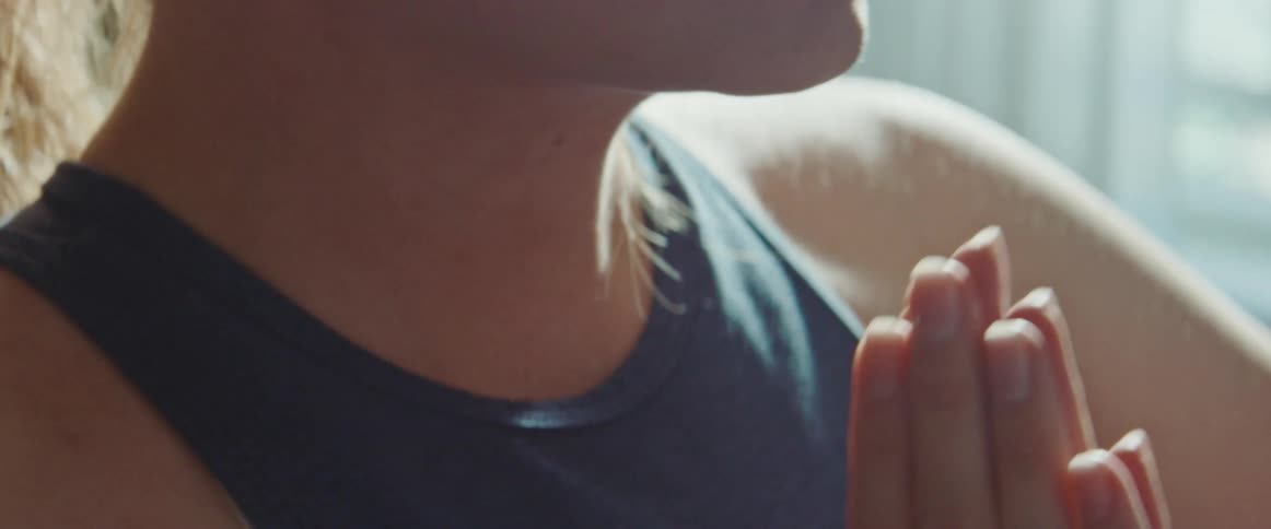 Woman standing near window stretches then places palms together at her chest