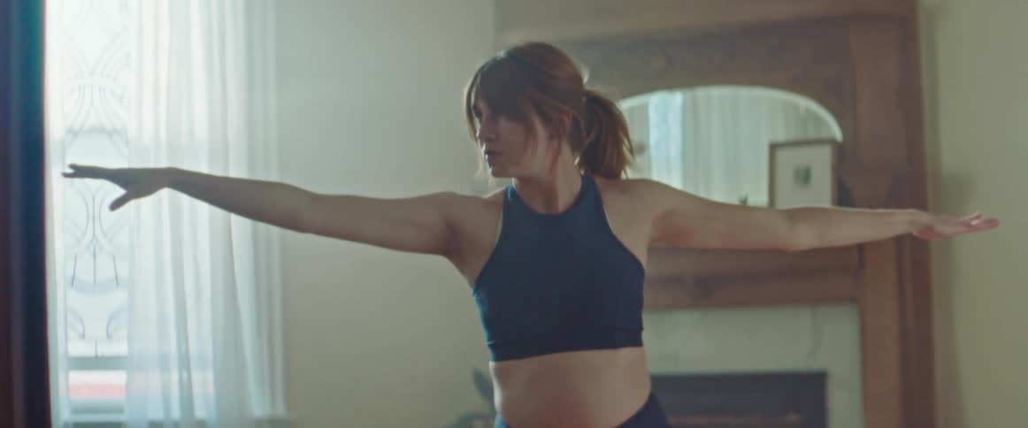 Pregnant woman with sport bra and a ponytail does stretching exercise on a pilates mat in the living room