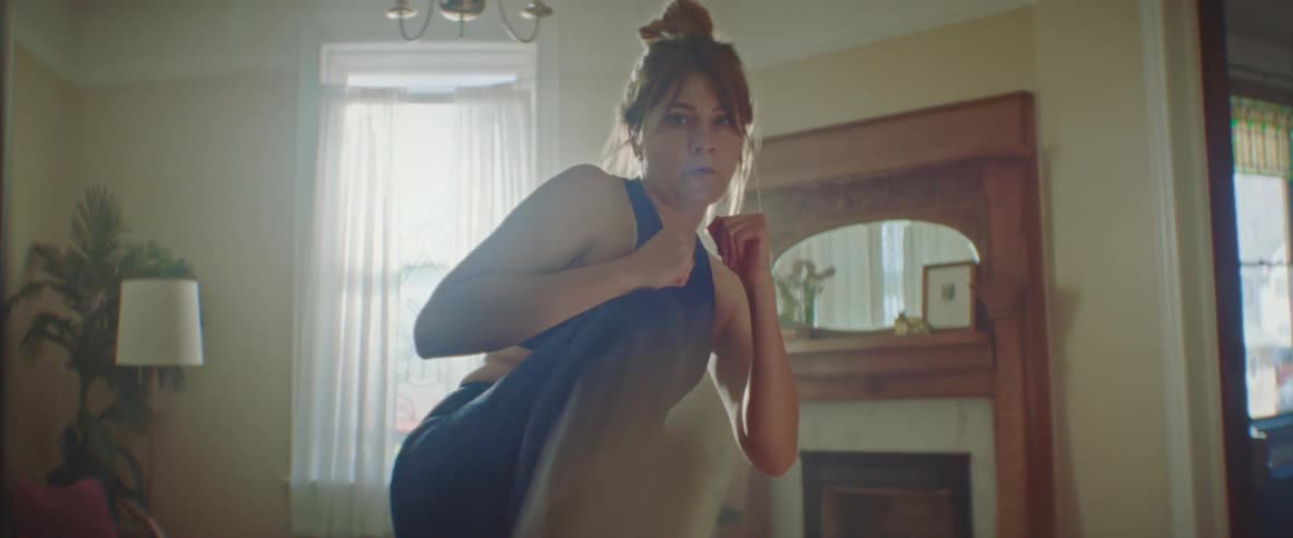 A woman does high kicks for exercise in her living room during the day