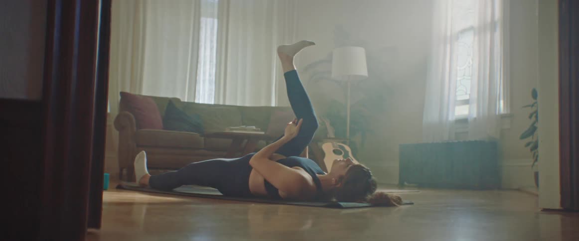 Pregnant woman with leggings and sport bra lies on a pilates mat and stretches her legs