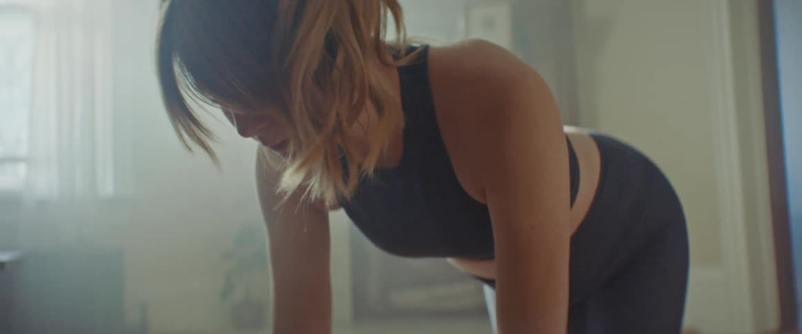 A young woman does yoga on a yoga mat in the living room of a house during the day