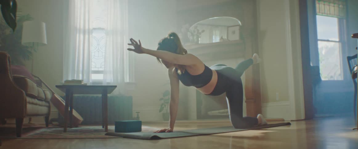 A young woman practices yoga on a yoga mat in her living room during the day