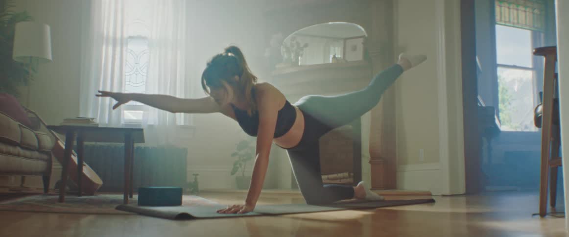 Woman with a ponytail sport top and leggings works out on a pilates mat in the living room at home