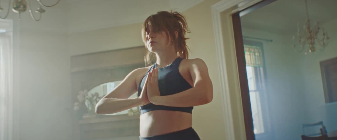 Pregnant woman does yoga as the sun shines through windows in the living room at home