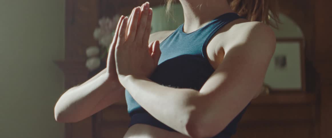 Pregnant woman with a ponytail and sport bra exercises as the sun shines through the windows in the living room