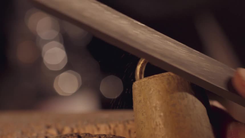 Person files a metal loop on top of a cylindrical object under soft lighting
