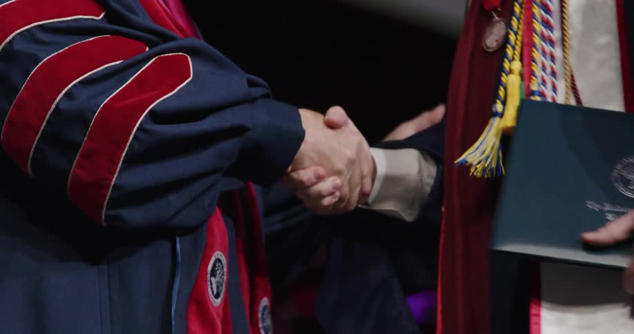 Closeup of the hands of a graduate in a gown greeting another
