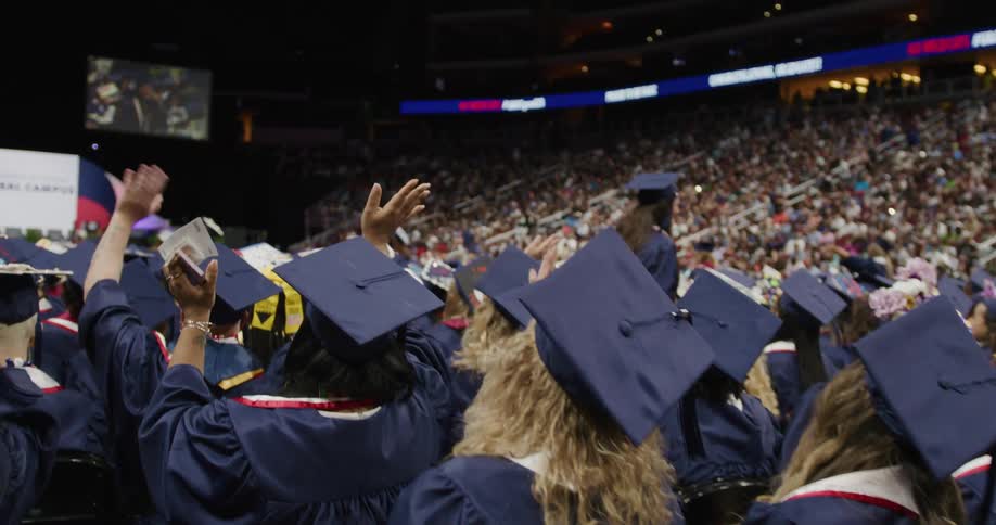 A huge crowd fills an arena to watch a university graduation ceremony