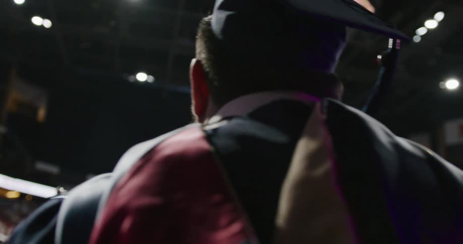 Person wearing graduation cap and gown walks on stage