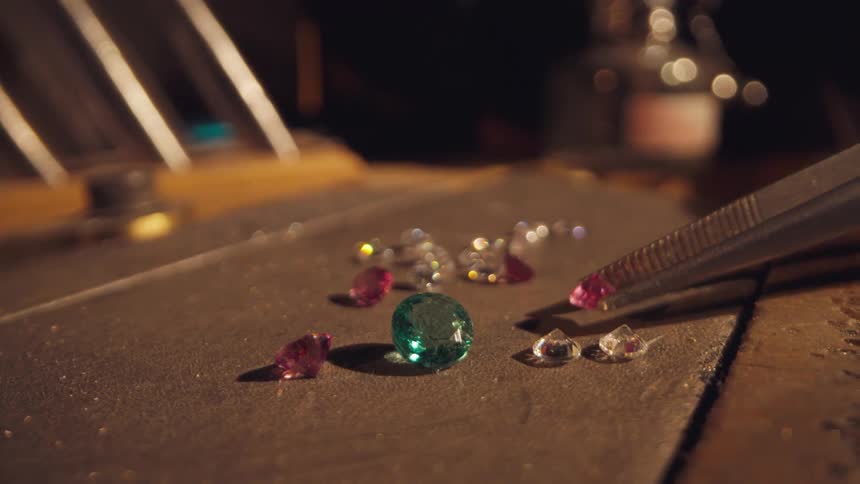 Tweezers picking up diamonds and moving them to a different spot on the table near other gems