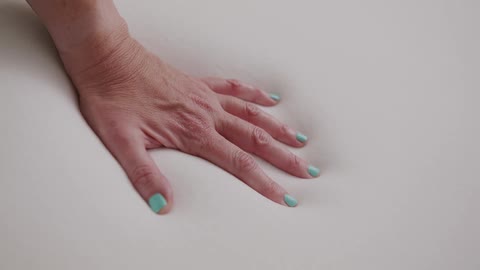 Hand with painted nails leaves imprint on soft memory foam mattress