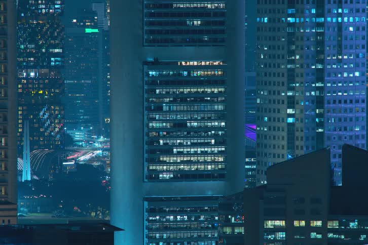 A time lapse of a tall building shows its interior lights turning on at night