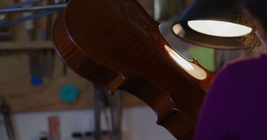 Woman with her back to the viewer with a lamp in front of her and holding a violin in her hand