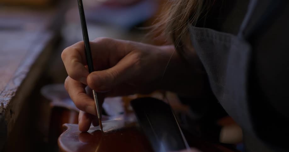 A female carefully uses a brush to paint accents onto the surface of a violin