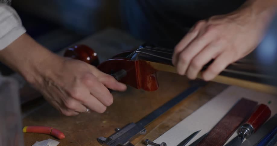 Persons hands make adjustment to neck of cello