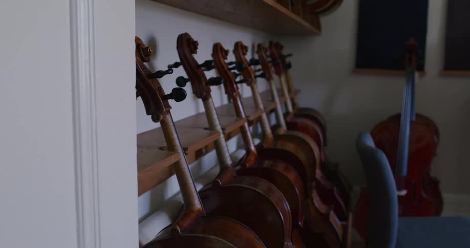 Row of cellos lean against wooden shelf