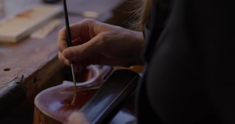 A woman is using a brush to put finish on a violin