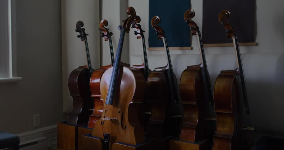 The cellos are stacked in a corner of the room wall