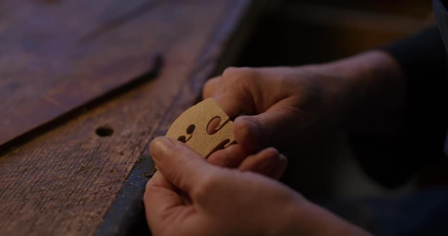 A hand of a person who is using a small and sharp tool to carve a wooden material