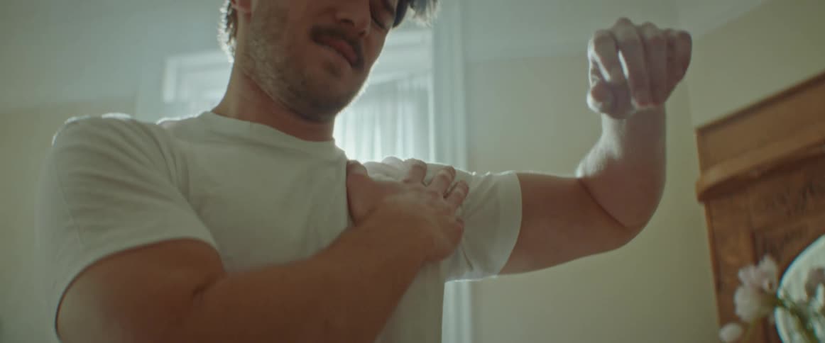 Man with a beard and an undershirt warms up for exercising in the living room at home