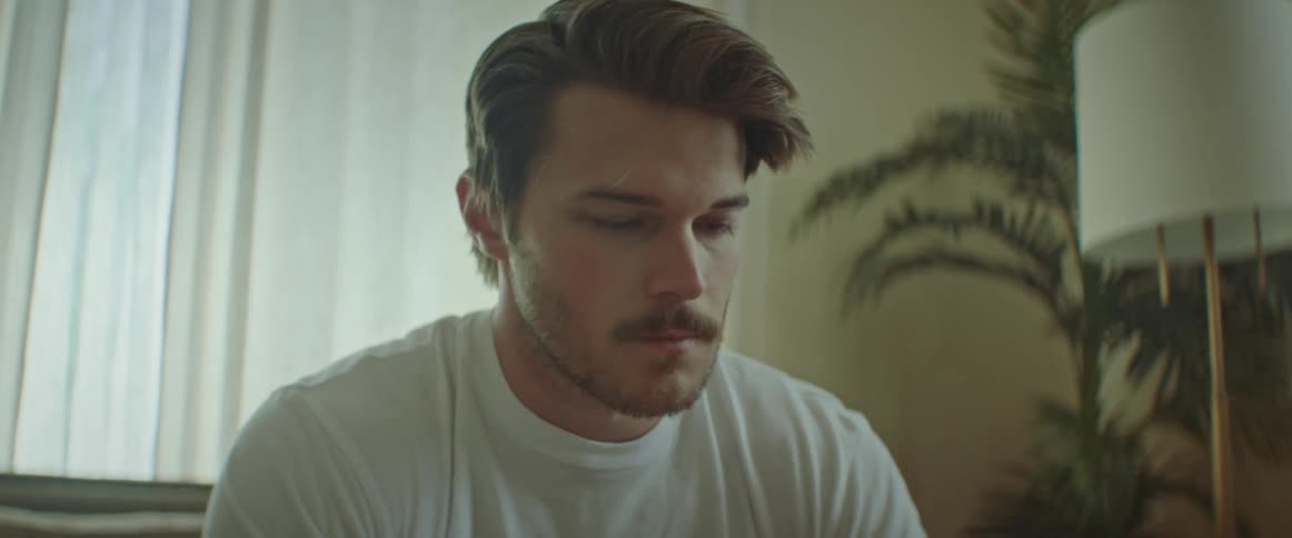A man opens a notebook while sitting on a sofa in the living room of a house