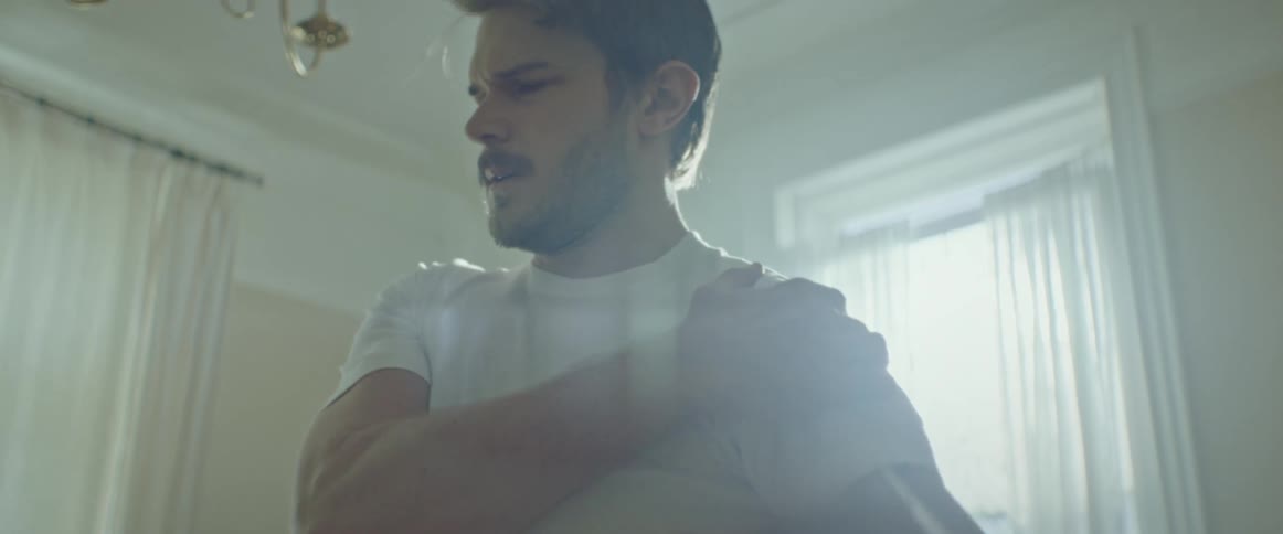 Man with a beard and a white t shirt stretches painful shoulder after injury