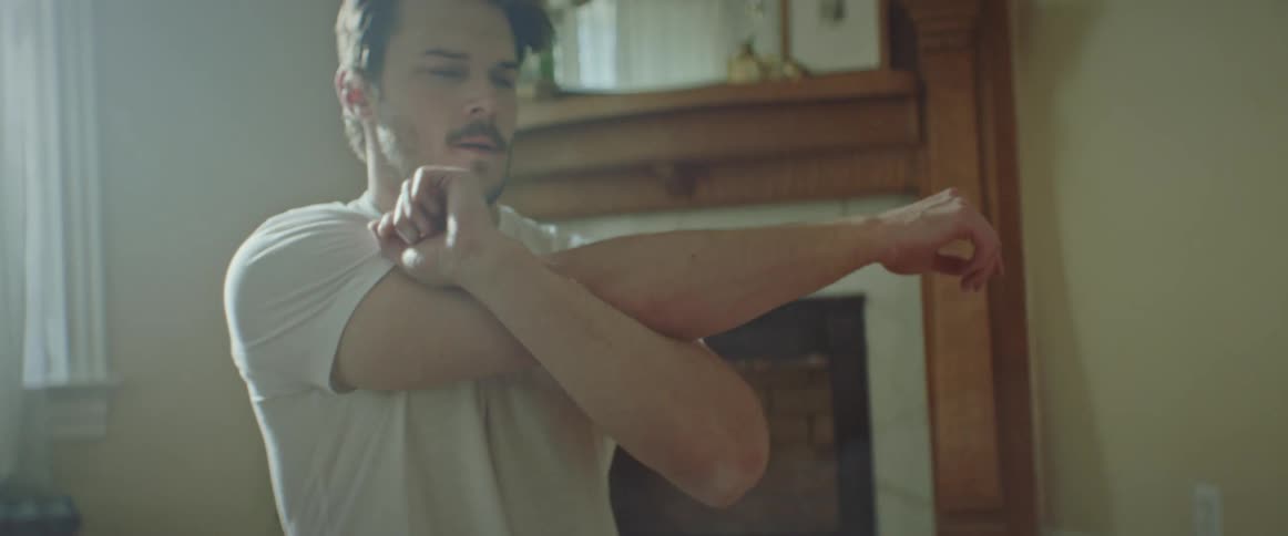 A man stands in his living room stretching his arm over his body