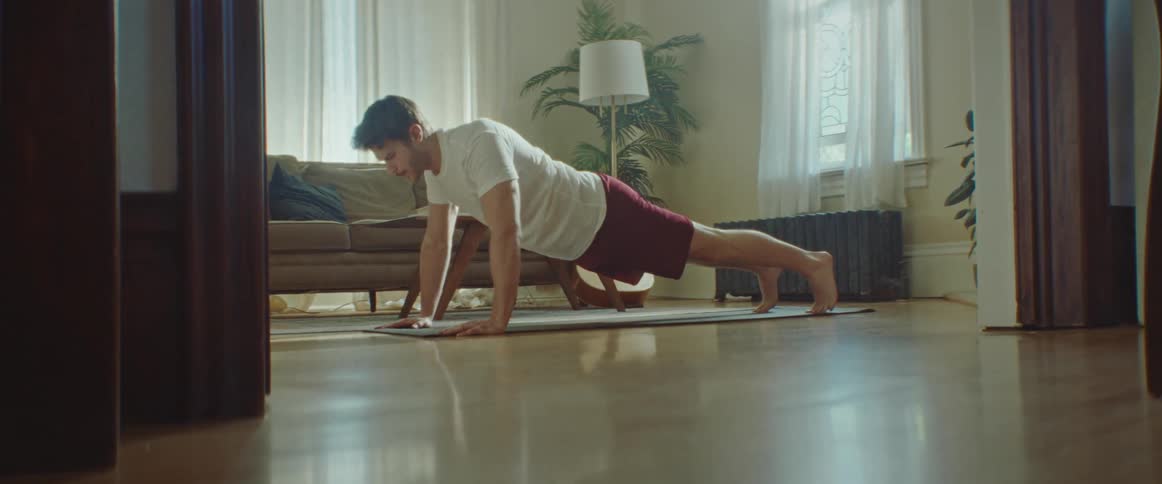 Man with a beard a white shirt and red shorts does push ups on a pilates mat in the living room at home