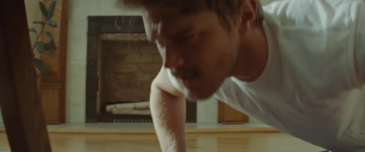 Man with a white t shirt and a beard does push ups on a pilates mat in the living room at home