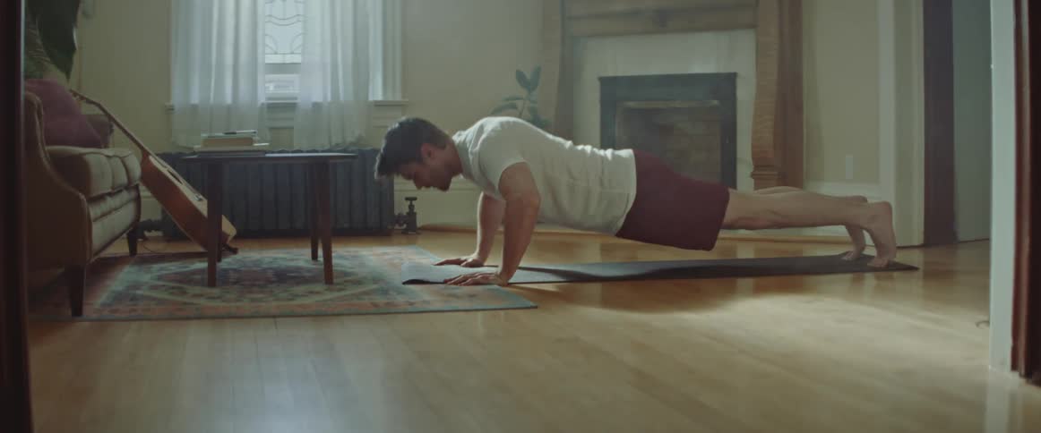 A man does pushups on the floor of his living room during the day