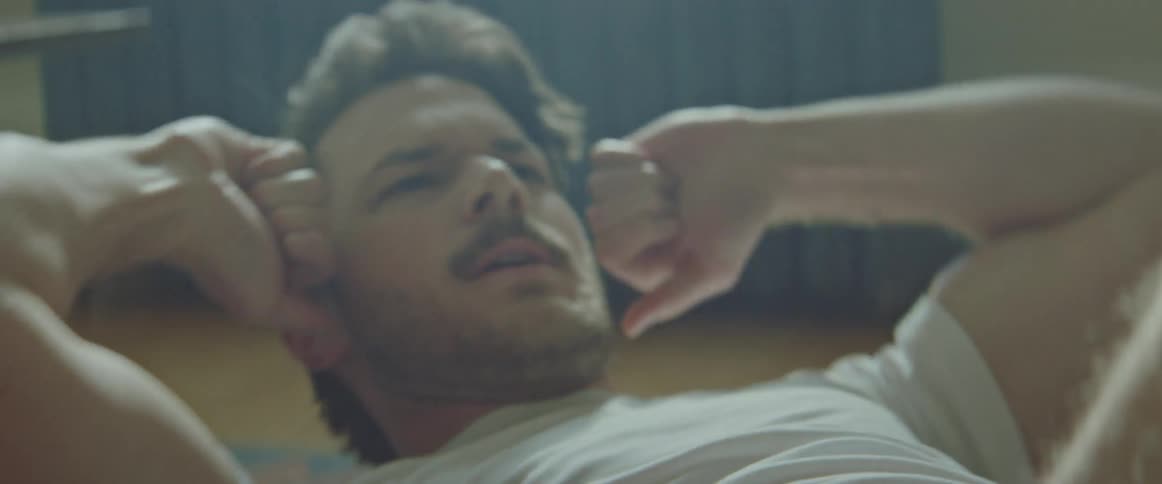 Man with a beard and a white undershirt does crunches in the living room at home