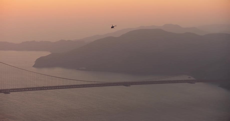 Aerial view of a helicopter flying over the San Francisco Bay and Golden Gate Bridge at dusk