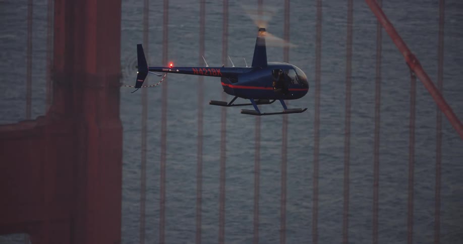 A small blue helicopter flying over the San Francisco Bay next to the Golden Gate Bridge