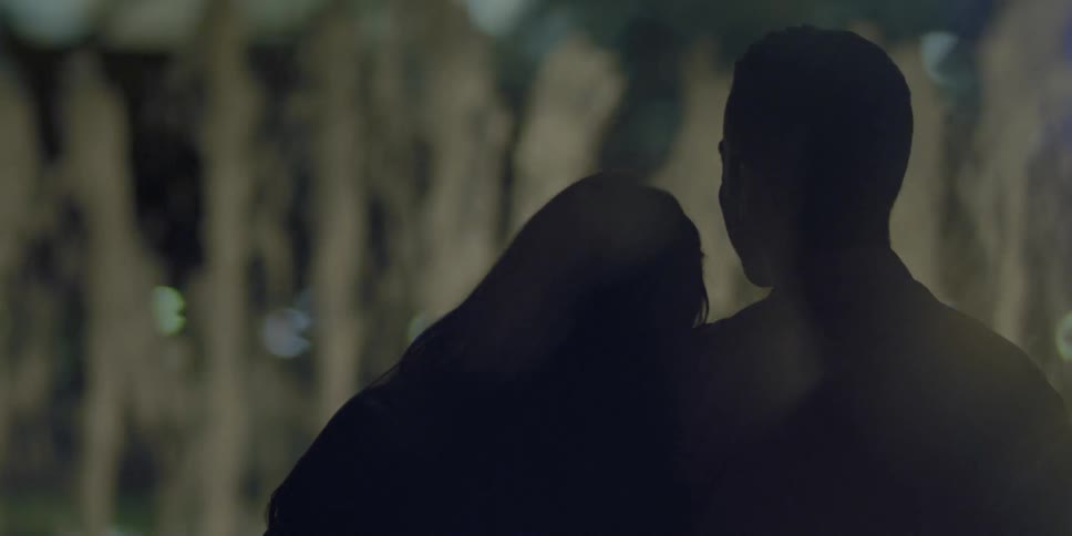 A man and woman lean against each other in front of a fountain