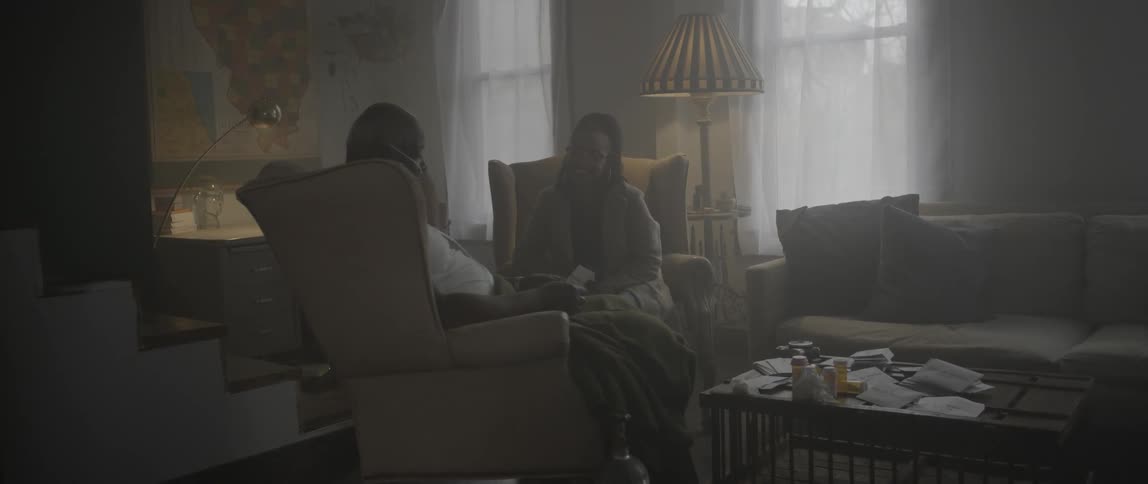 A man and woman talk together in a dark living room