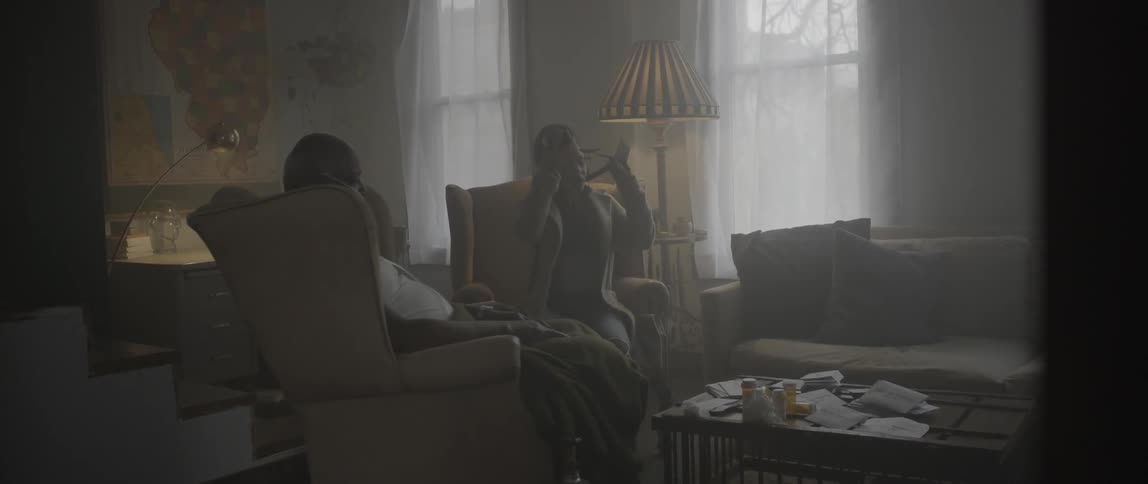 A woman sits in a chair next to another woman and takes off a camera