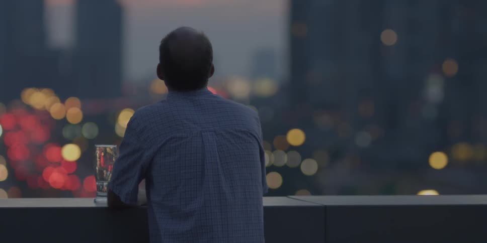 Man looks out at a city at dusk