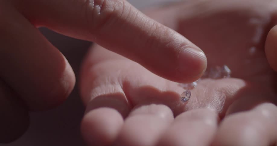 A person holds small gems in their hand and pushes them around