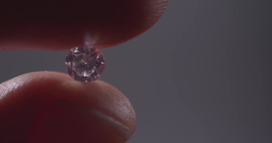 A person rolls a diamond in between their fingers