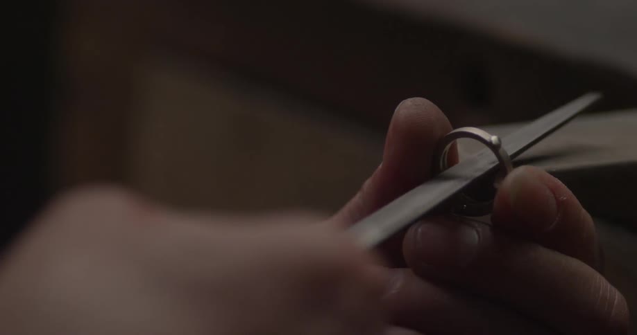 A person holding a ring and smoothing the inside with a file