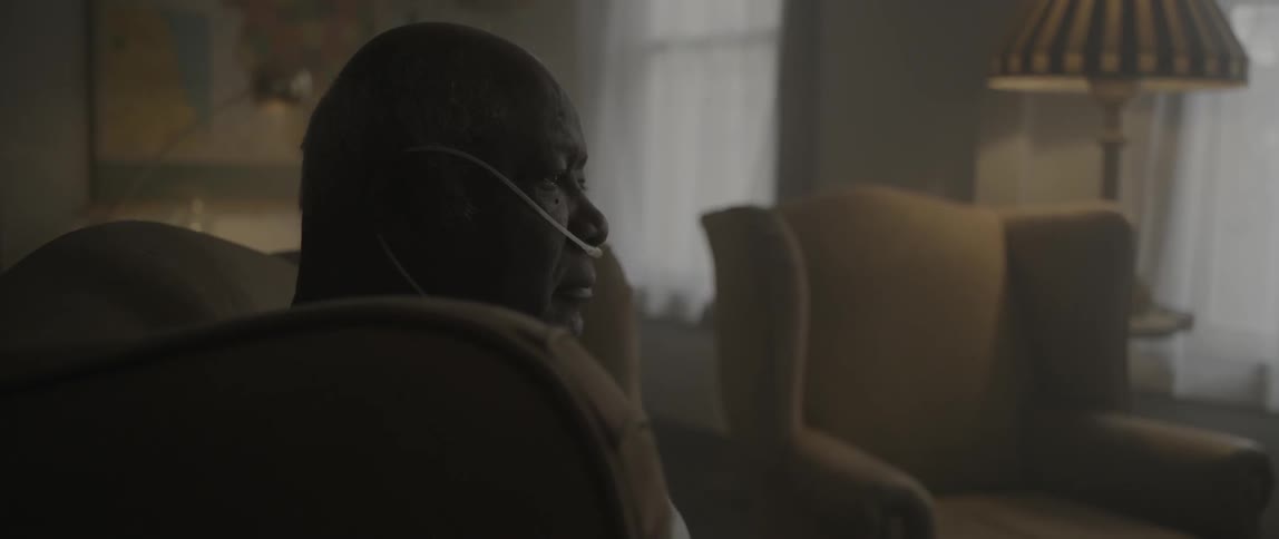 A man wearing an oxygen tube sits in a light colored chair